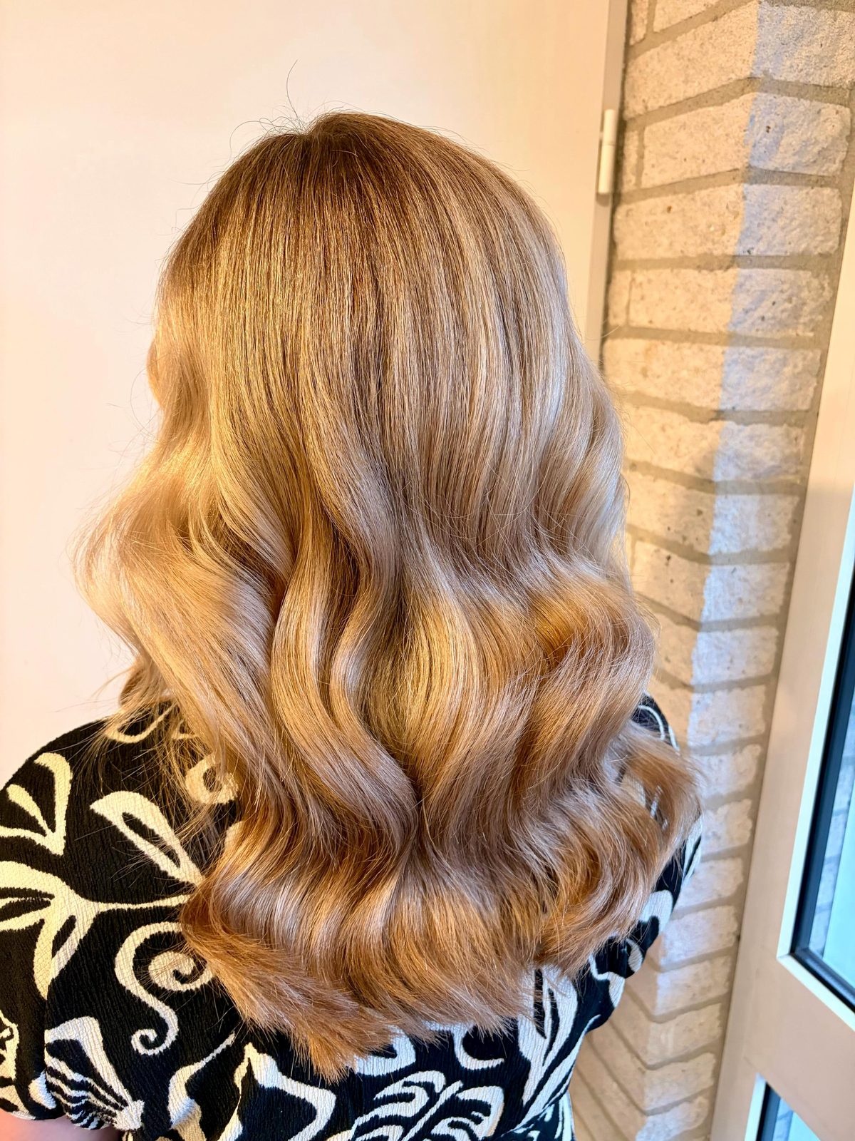 Lang haar in warme blonde golven, van achteren gezien, in de salon