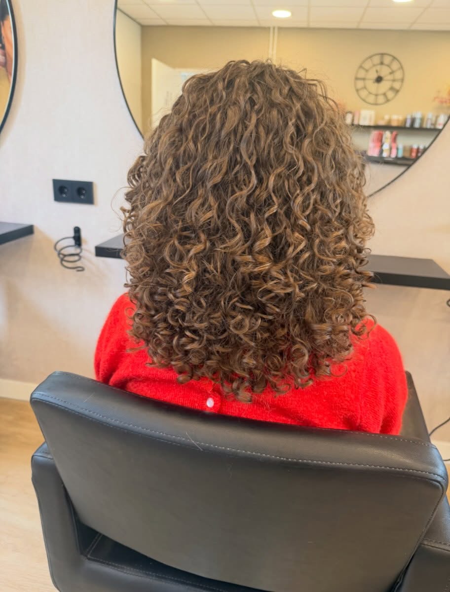 Bruine krullen na een curls cut, op de stoel voor de ronde spiegel